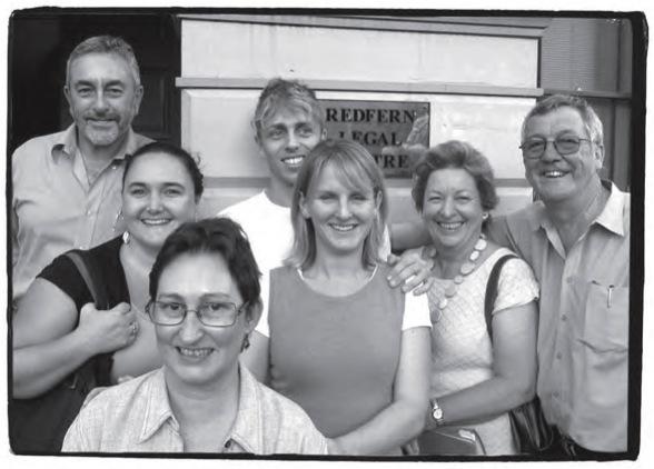 A group of people stand smiling outside a building with a gold plaque that reads 'Redfern Legal Centre' 