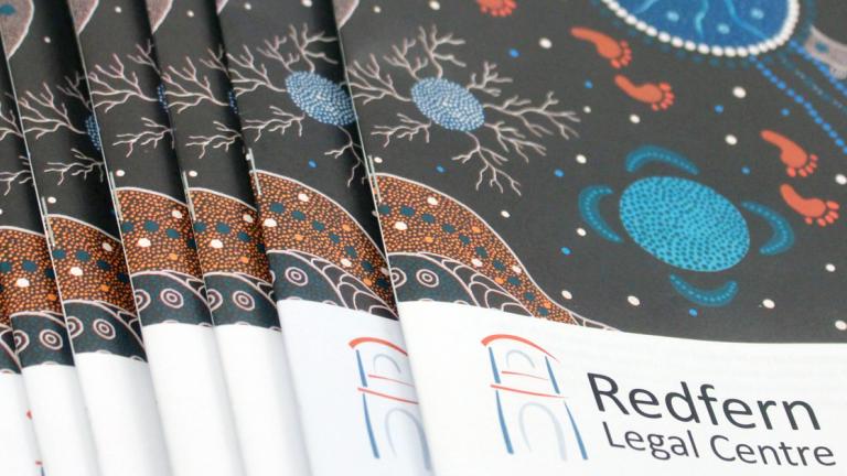 reports stread out on a table with a black green and orange Aboriginal design on the cover and the words RedFern Legal Centre on the cover