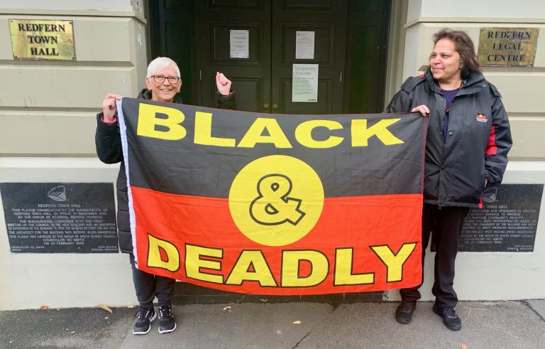 Two women holding an Aboriginal flag that says 'Black and Deadly'