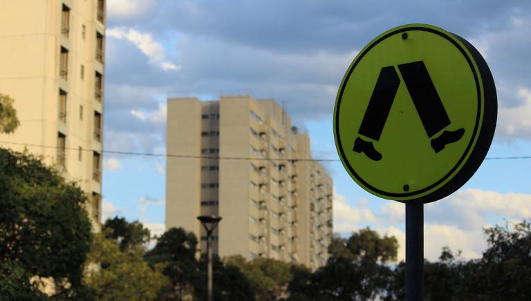 two apartment block in the distance against a blue cloudy sky. In the foreground is a black and yellow zebra crossing sign.