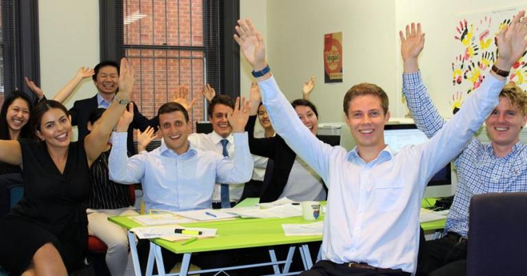 Group of university students excitedly raising arms while seating