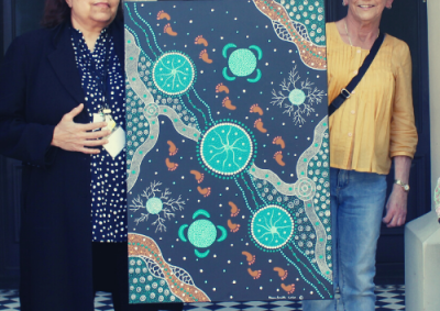 Two women stand either side of a black green and orange Aboriginal painting