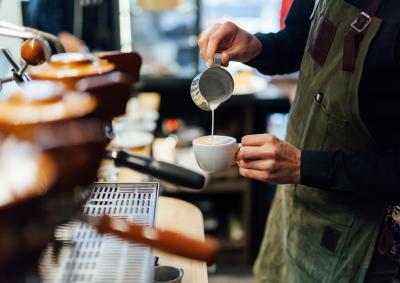 Close up a barista hands pouring milk from a silver jug into a cup ofcoffee