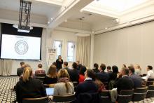 Group of people watching a woman delivering a PowerPoint presentation