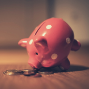 Closeup of a pink piggybank with some coins next to it on a wooden table