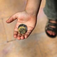 Child holds out hand containing silver and gold coins