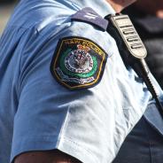 Close-up of a police officer walking along the street, showing their shoulder emblem